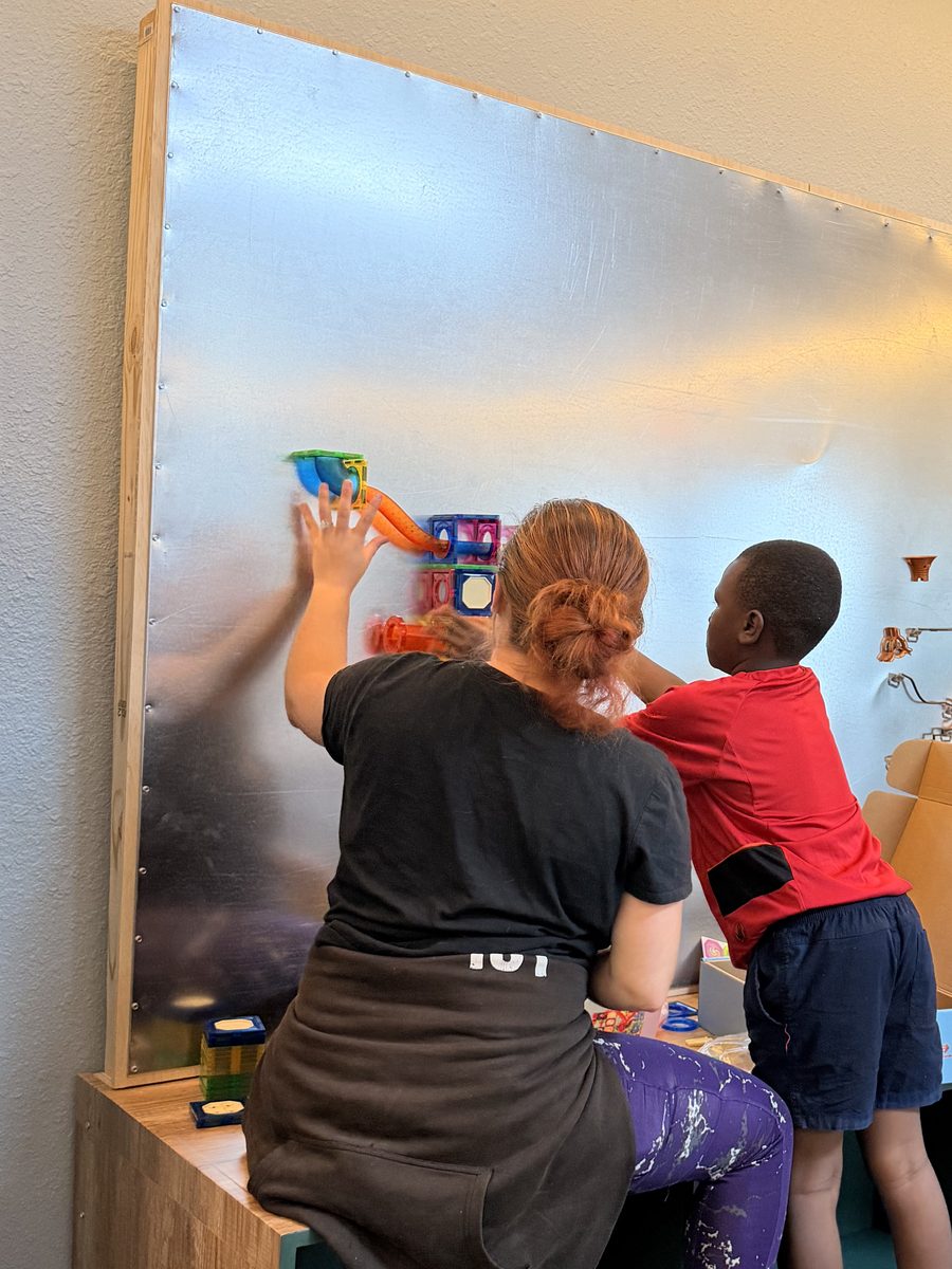 A Creative Learning therapist and a child building together on the magnetic wall in the Cocoa center